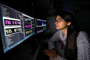A woman looks at information on two computer monitors
