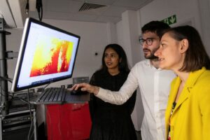 Photo of three people looking at a computer monitor in a darkened room